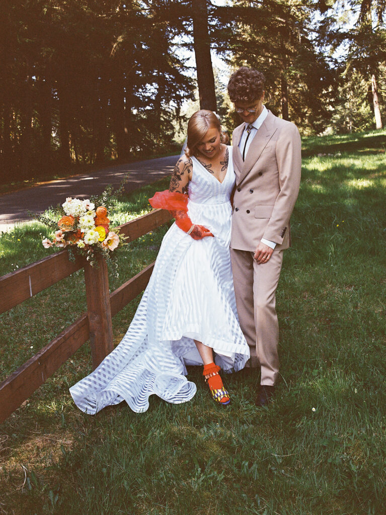 An editorial style photo of a groom standing next to his bride in a white gown showing off her vibrant orange accessories in a photo taken by washington state wedding photographers 