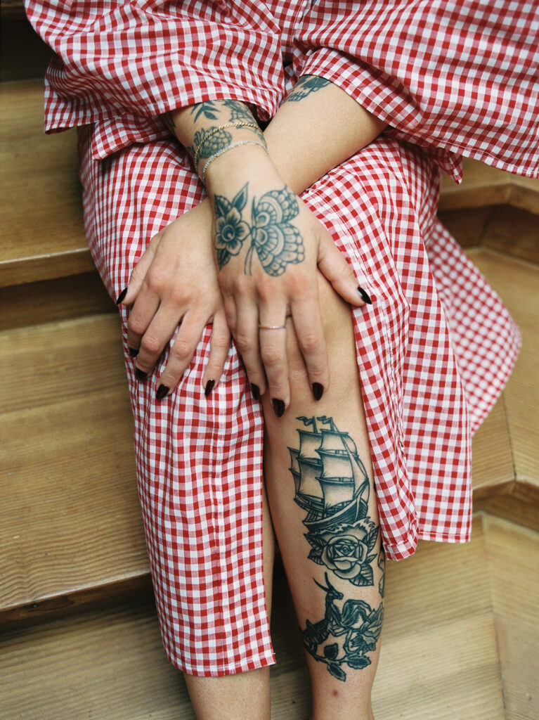 A closeup of a bride's tattoos and nails with her hands folded on her red & white gingham plaid robe as she gets ready for her Vashon wedding 