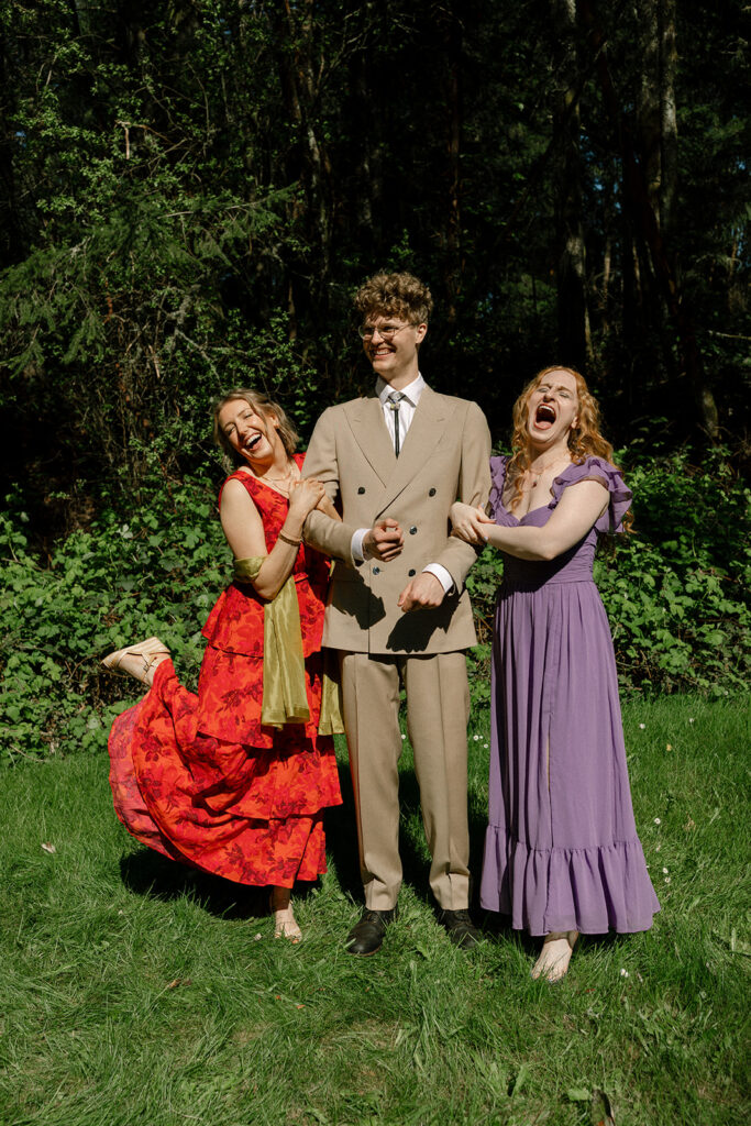 A Washington groom wearing a tan suit and bolo tie laughs alongside two guests at his Vashon Island wedding 