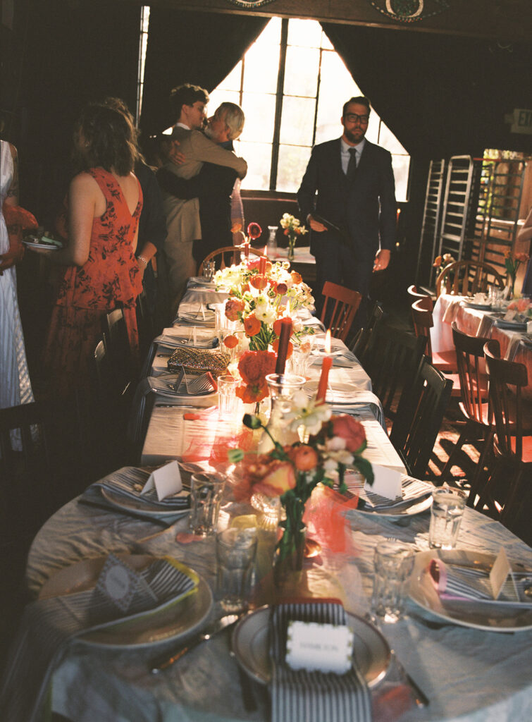 A table decorated in vibrant florals and orange tapered candles is shown at a whimsical wedding reception held at snapdragon vashon