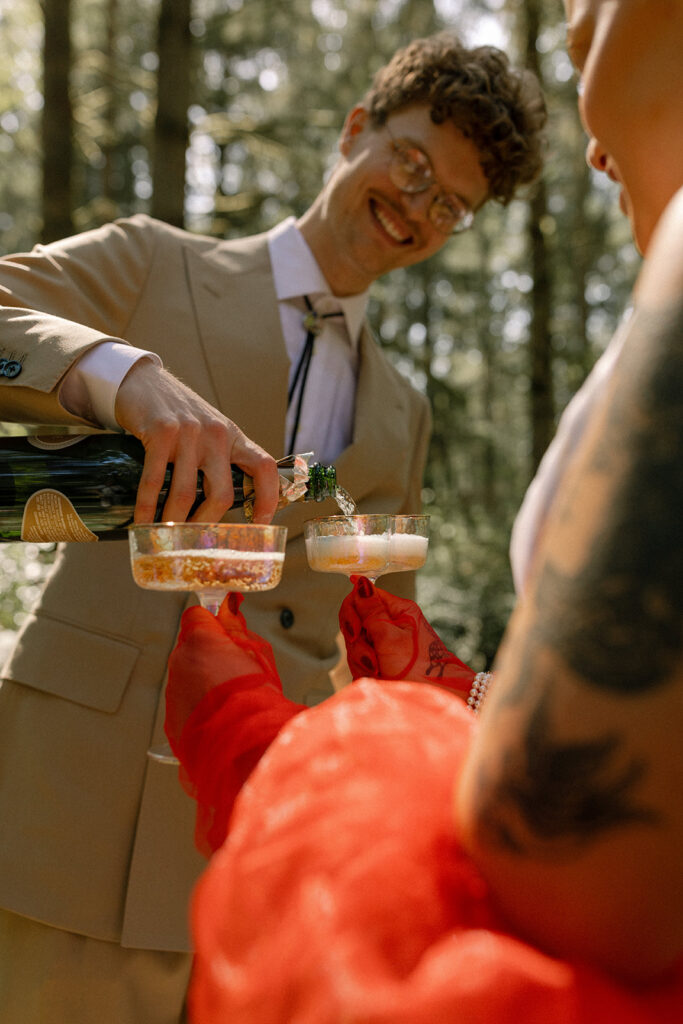 A WA groom in a tan suit pours champagne for himself and his newbride at their Vashon Island wedding 