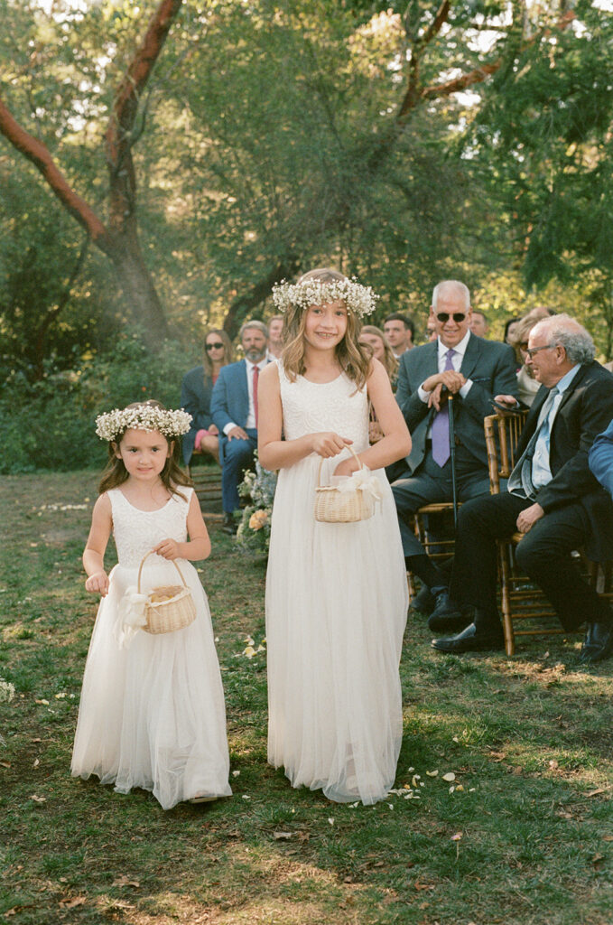 Flower girls wearing white spread petals down the aisle of a wedding at Captain Whidbey Inn Coupeville WA
