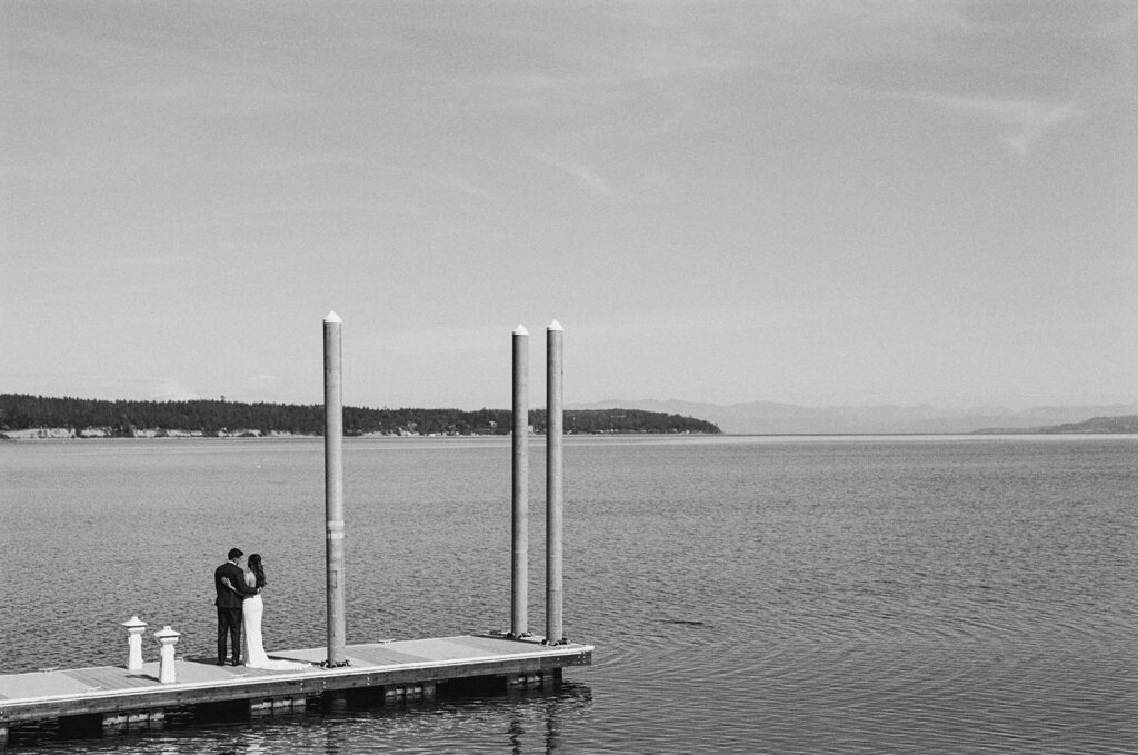 A black and white image of newlyweds embracing on the dock overlooking the water at their captain whidbey inn wedding