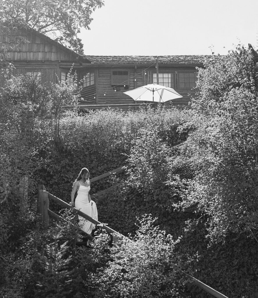 A bride holds up her dress as she walks down steps in a b+w image taken at her captain whidbey inn wedding