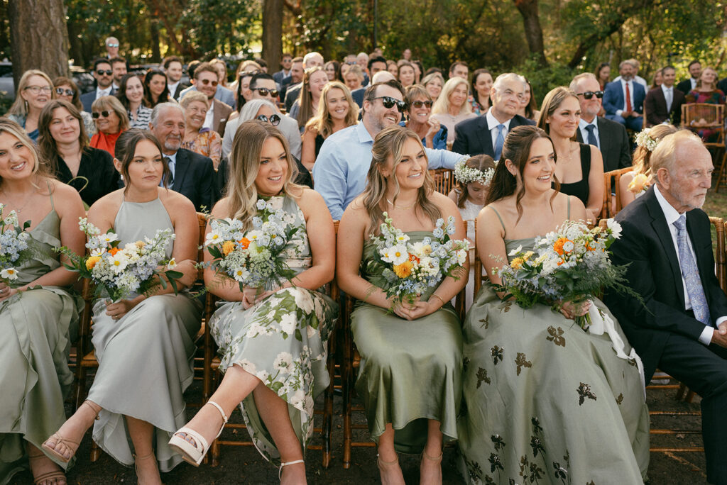 Bridesmaids wearing sage green dresses look on from the front row of a Captain Whidbey wedding