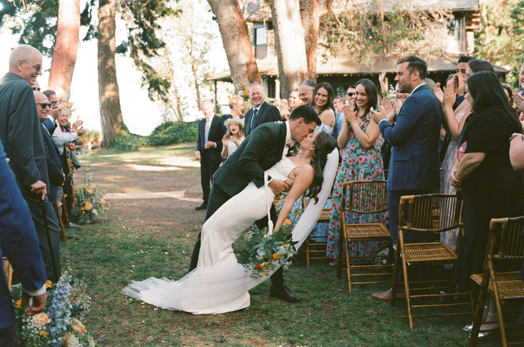 Newlyweds share a dip kiss at the end of the aisle following their wedding ceremony at Captain Whidbey Inn in Coupeville WA