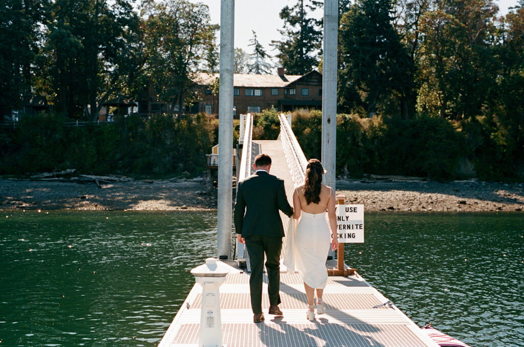 A bride and groom in their wedding attire walk side-by-side across a dock at Captain Whidbey Inn in Coupeville WA