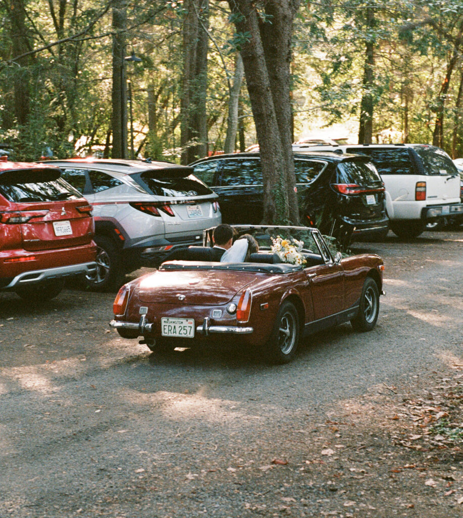A bride and groom leave their Whidbey Island wedding in a two seater vintage convertible 