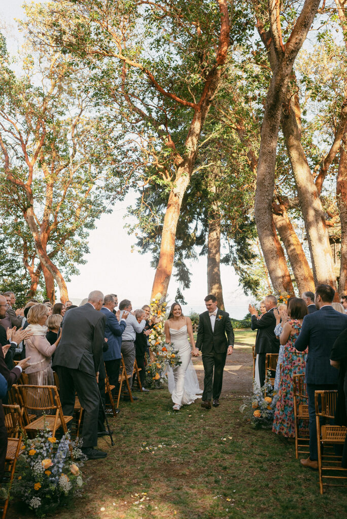 Newlyweds smile walking hand-in-hand down the aisle at their Captain Whidbey Wedding