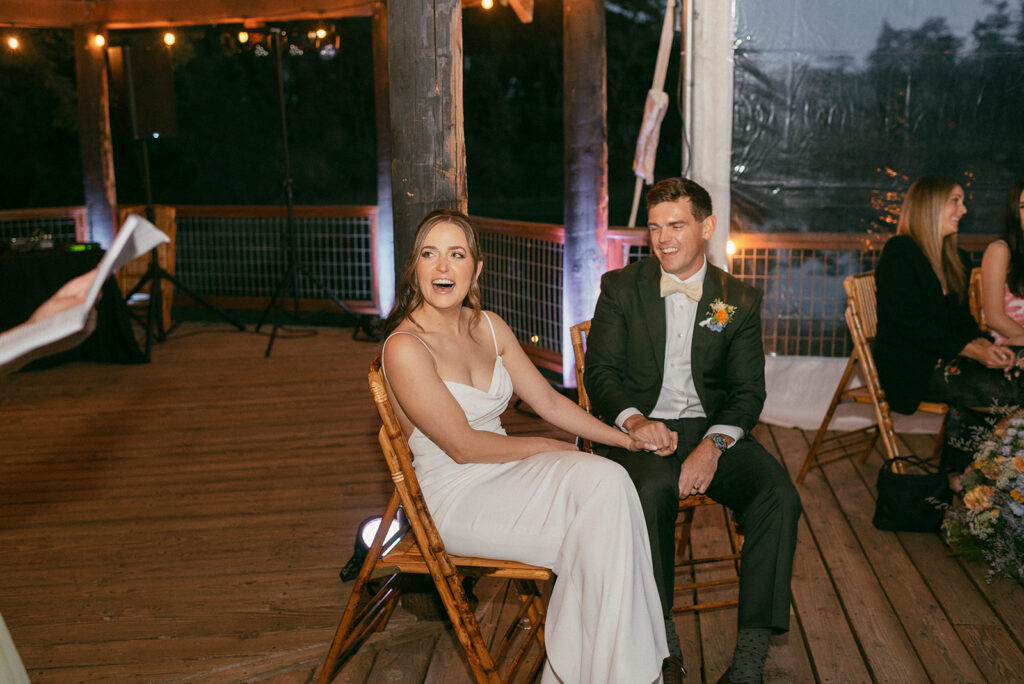 A bride and groom laugh as they listen to a speech from a guest at their Captain Whidbey Inn wedding