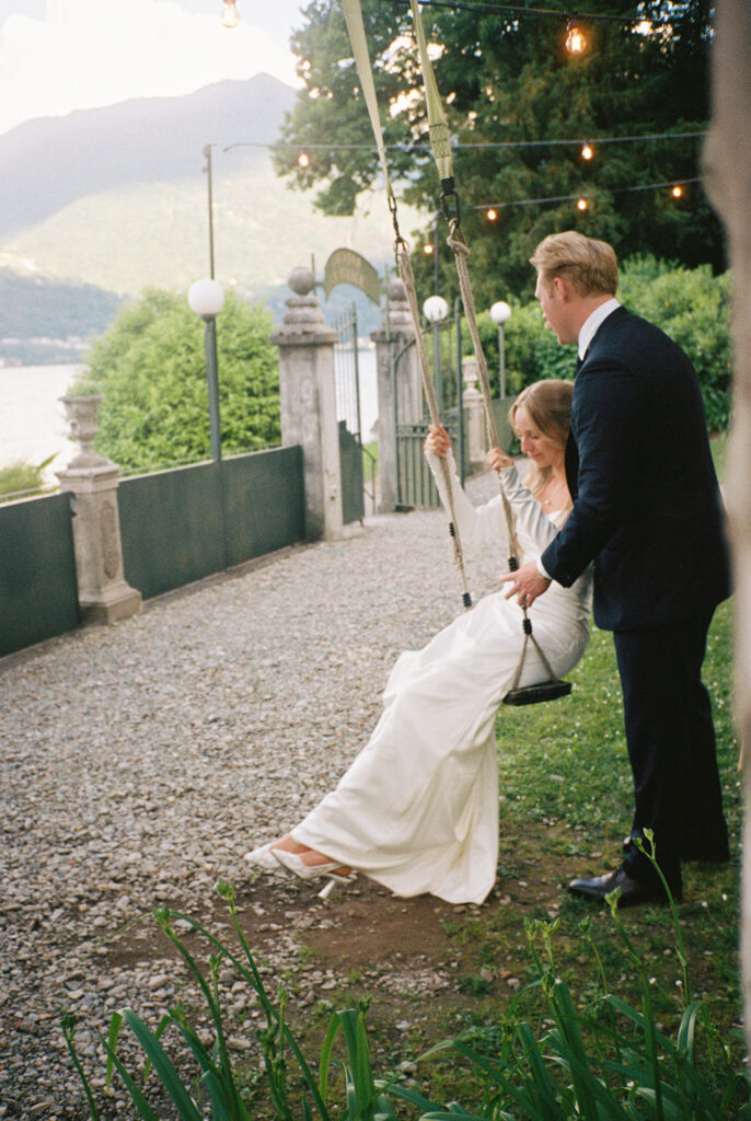 A groom pushes his bride in a white dress on a rope swing at their destination wedding at Villa la Felice 