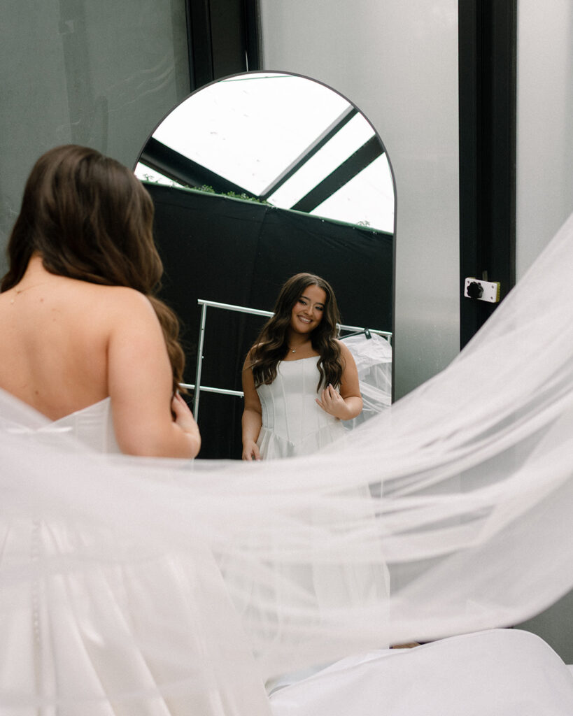 A bride smiles into an arch mirror as she gets ready for her Bavarian Downs wedding in Chaska MN