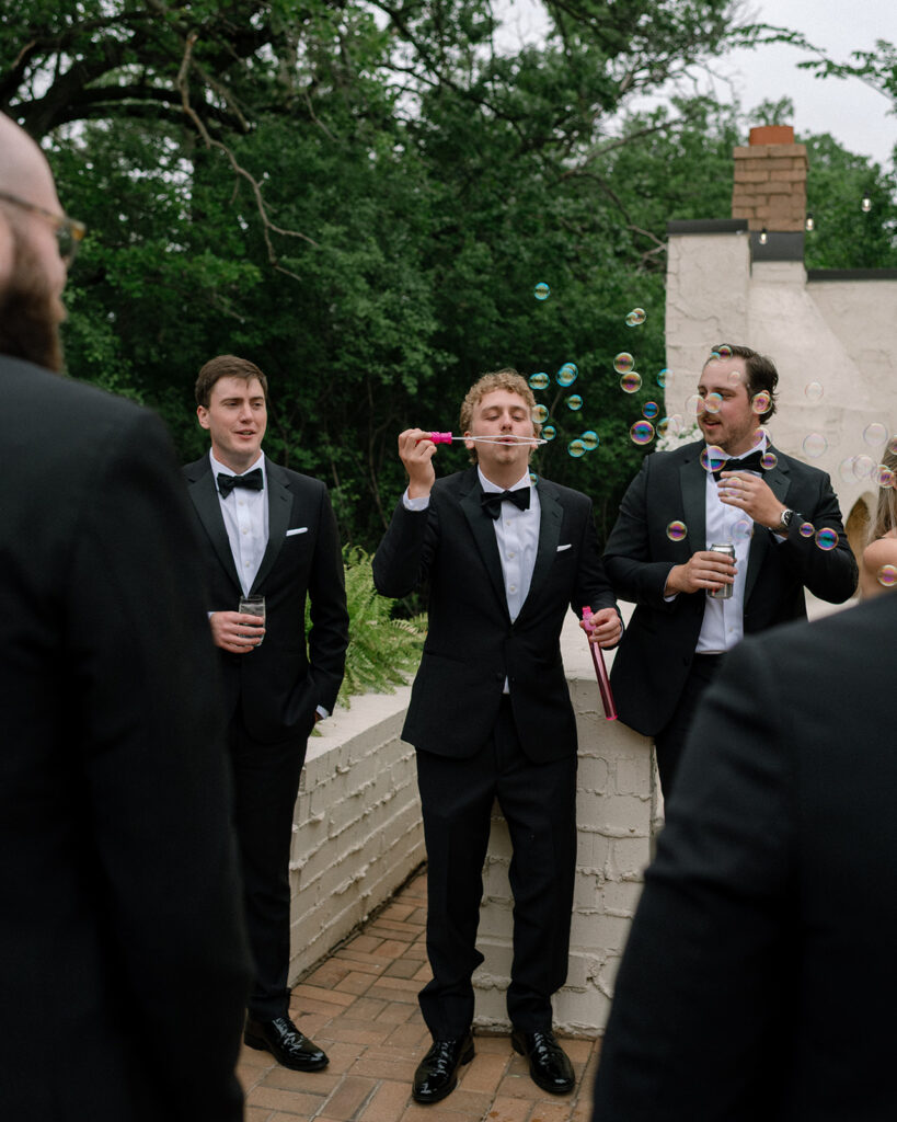 Groomsmen in black tuxes blow bubbles following a bavaria downs chaska wedding 