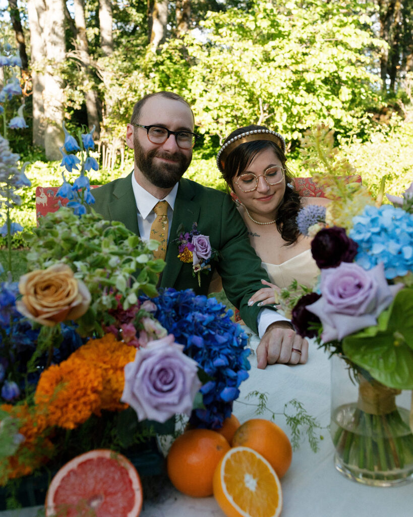 A bride and groom smile at their wedding reception, surrounded by colorful florals at the griffin house in hood river, oregon