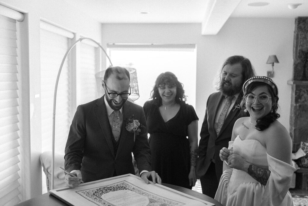 A b+w photo depicts a wedding party and a bride and groom signing their marriage license at a hood river wedding at the griffin hous