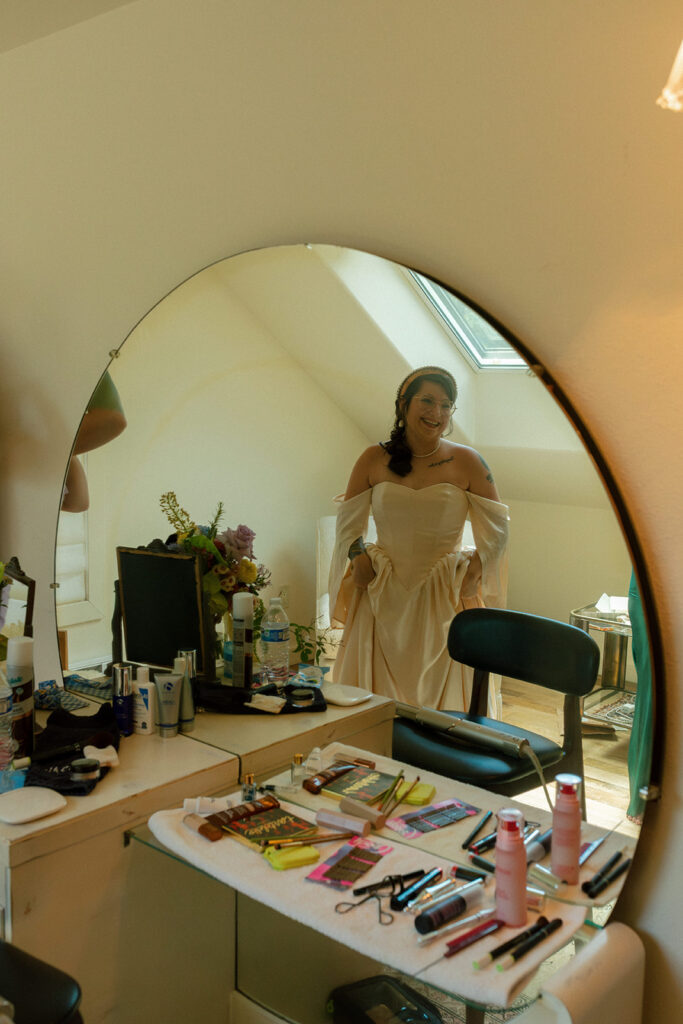 A bride smiles into a mirror in one of the getting ready suites at griffin house hood river