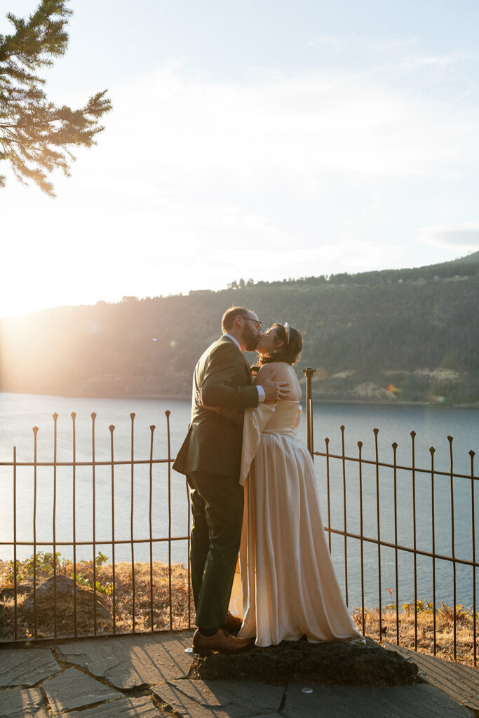 Newlyweds share a kiss in their wedding attire overlooking Columbia River Gorge at their hood river oregon wedding