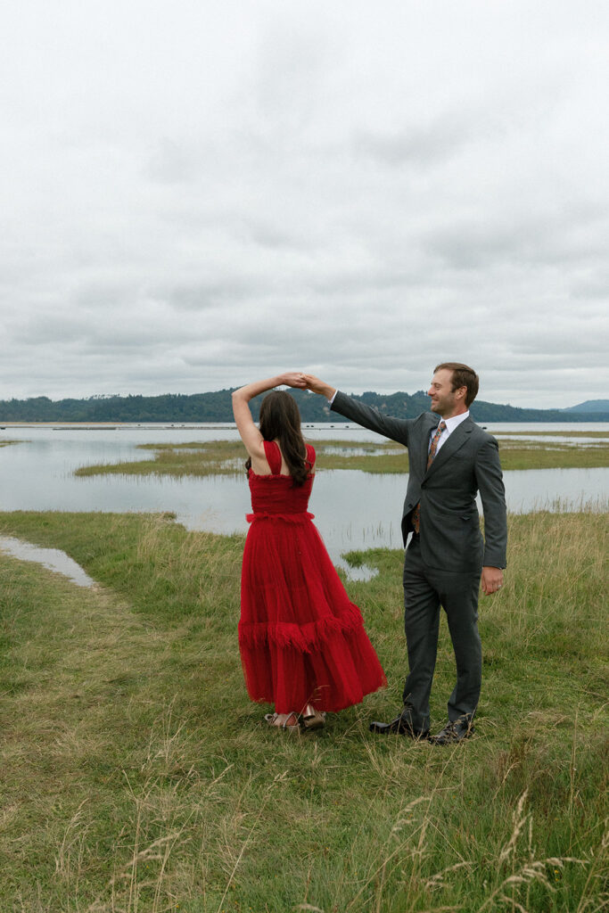 A groom in a charcoal suit twirls his bride in a vibrant red dress after their  Washington wedding at The Tokeland Hotel 