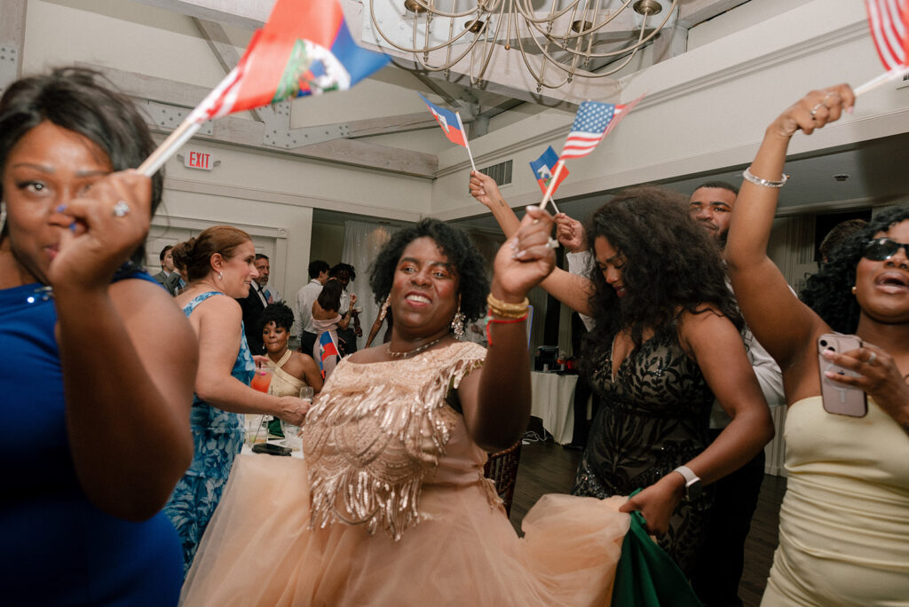 Wedding guests wave Haitian and American flags at a multicultural New England wedding reception 