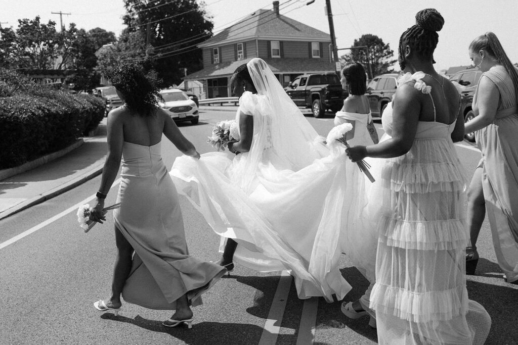 Bridesmaids help carry the train of a bride's gown for bridal photos taken  by a New England wedding photographer 