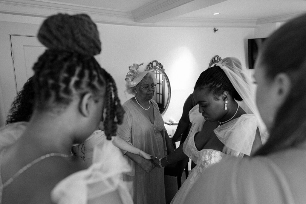A bride is surrounded by family in the bridal suite as they pray over her before her New England Wedding at Barker House in Scituate MA