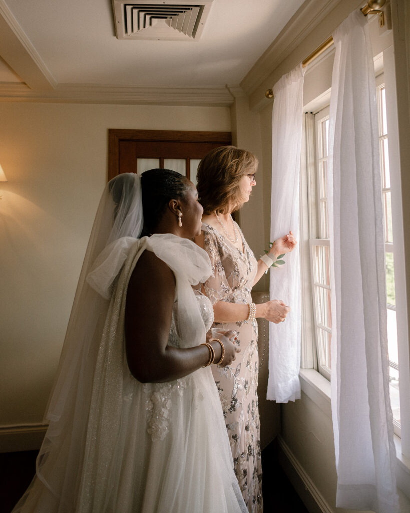 A bride and her soon-to-be MIL gaze out the window of the bridal suite at her barker tavern wedding