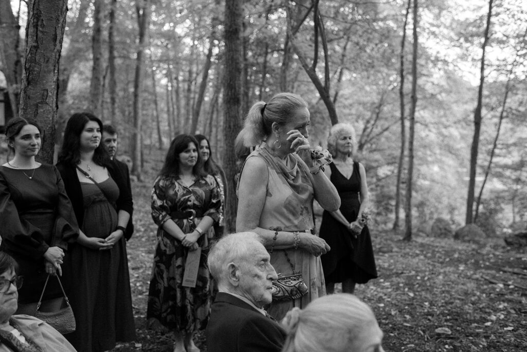 A black and white image depicts wedding guests getting emotional during a ceremony held at mountain lakes park in ny