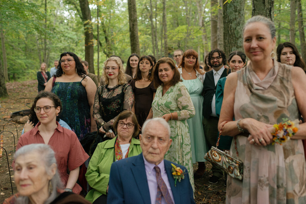 Wedding guests smile as they observe a ceremony in the forest at mountain lakes park westchester